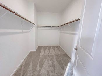 a walk in closet with white walls and a gray carpet